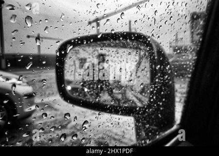 Pompe à essence attendant à travers les gouttes de pluie rétroviseur humide - voiture et transport relié Photographie noir et blanc des beaux-arts Banque D'Images