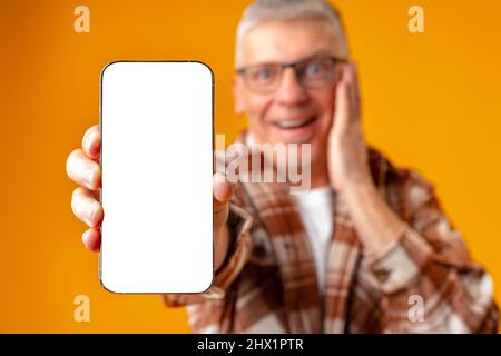 Photo de l'homme surprise senior pointe le doigt sur le smartphone sur fond jaune Banque D'Images