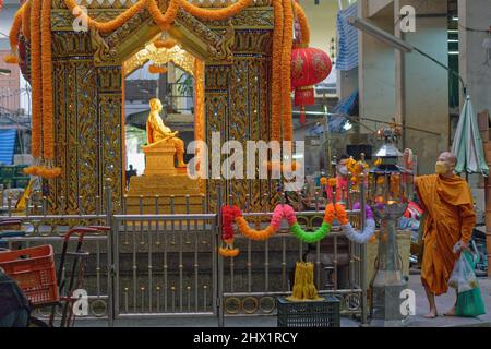 Au Pak Klong Talat (marché) à Bangkok, en Thaïlande, un moine arrange des fleurs dans un sanctuaire en l'honneur d'un ancien officiel considéré comme l'esprit gardien du marché Banque D'Images