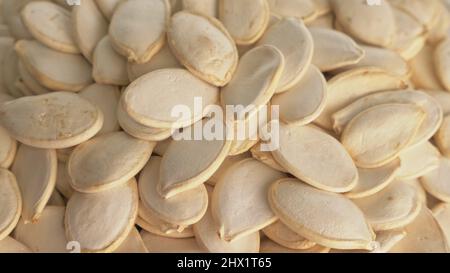 Les noix de citrouille non pelées tournent sur une table dans une assiette. Les en-cas dans un plat transparent sur un fond blanc isolé tournent en mouvement. Une alimentation riche en protéines, délicieuse et saine. Banque D'Images