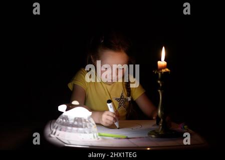 Une petite fille dessine des personnages de fantaisie près d'une bougie dans une pièce sombre. Enfant faisant ce qu'il préfère lors d'une panne de courant. Banque D'Images