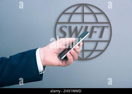 MOSCOU - MARS 04: Un homme d'affaires habillé en costume tenant smartphone devant le logotype SWIFT sur un mur à Moscou, Mars 04. 2022 en Russie Banque D'Images