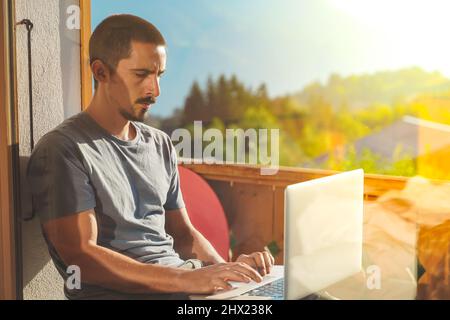 Jeune homme travaillant avec un ordinateur portable sur un magnifique paysage de montagne. Un homme attrayant qui travaille. Indépendant. Voyageur. Banque D'Images
