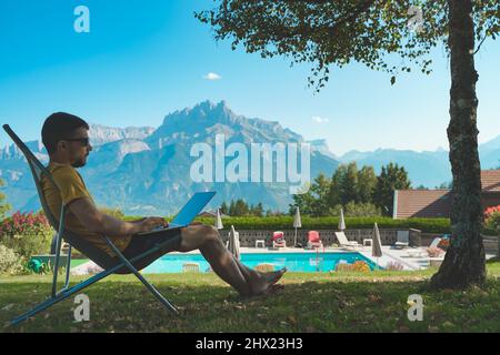 Jeune homme travaillant avec un ordinateur portable sur un magnifique paysage de montagne. Un homme attrayant qui travaille. Indépendant. Voyageur. Banque D'Images