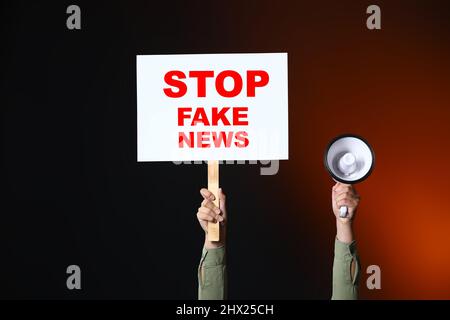 Femme tenant le mégaphone et la plaque avec le texte ARRÊTER LES FAUSSES NOUVELLES sur fond sombre Banque D'Images