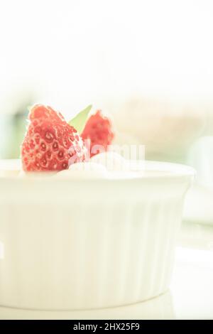 Crème brûlée ou crème brûlée avec garniture de fraise sur une tasse blanche, blanc flou en arrière-plan. Gros plan. Banque D'Images