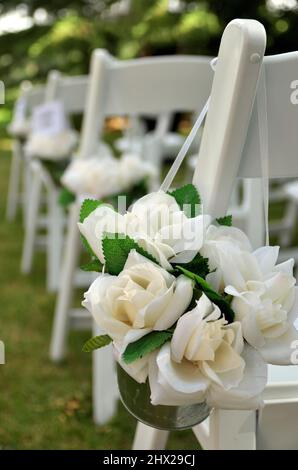 Des chaises blanches ornées de bouquets de roses en tissu blanc vous attendent lors d'un mariage dans le jardin Banque D'Images