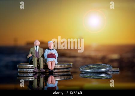 Couple âgé âge d'or inflation Pensions assis pile de pièces coucher de soleil miniature personnes Figures contexte Banque D'Images