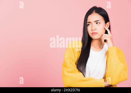 Portrait asiatique belle jeune femme debout menton poignée détendue penser à quelque chose à la question studio tourné isolé sur fond rose, Banque D'Images