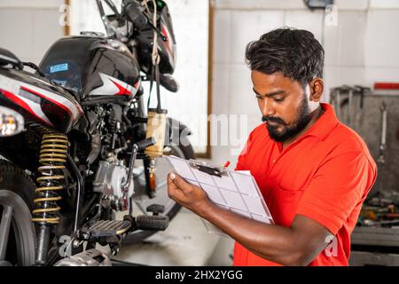 mécanicien occupé à noter les pièces de réparation de vélo pendant la réparation d'entretien au grage pour la facturation de client - concept d'occupation professionnelle, homme de réparation Banque D'Images