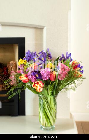 Un bouquet de fleurs printanières assorties, disposées dans un vase en verre et placé sur un feu de marbre dans une maison Banque D'Images