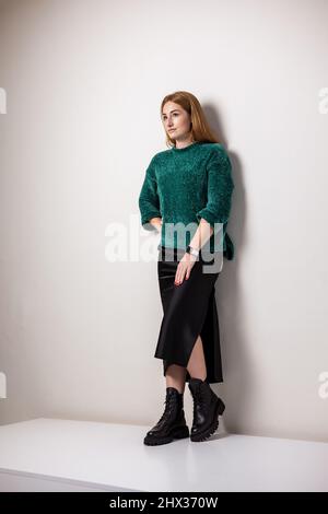 Une femme dans un pull vert chaud et une jupe noire dans des bottes en cuir noir. Tenue automnale tendance. Banque D'Images