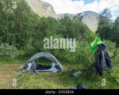 Petite tente ouverte avec sac à dos et matériel de randonnée en Laponie suédoise Paysage avec collines vertes, montagne et forêt de bouleau au sentier de randonnée Padjelantaleden Banque D'Images