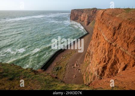 De hautes falaises rouges spectaculaires de l'île d'Heligoland avec mer rugueuse. Jour d'hiver ensoleillé et venteux à Helgoland, en mer du Nord, en Allemagne. Banque D'Images