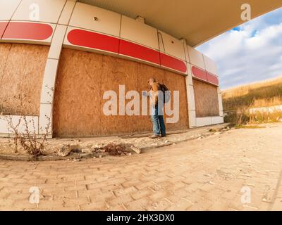 Homme en casquette avec sac à dos à la station-service abandonnée. Recherche et examen des stations-service abandonnées Banque D'Images