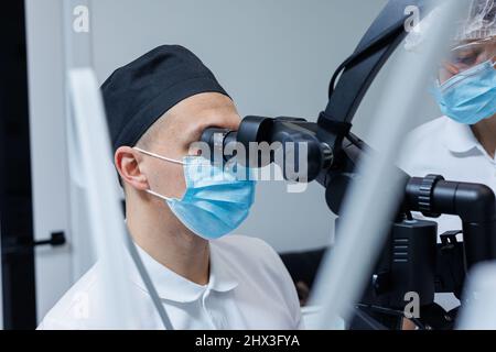 Un dentiste qui réussit à examiner les dents du patient avec un microscope dentaire tient les instruments dentaires près de sa bouche. L'assistant aide le médecin Banque D'Images