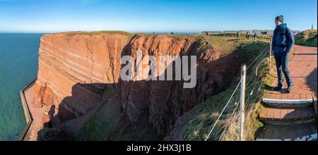 Femme debout sur le bord de hautes falaises rouges spectaculaires de l'île d'Heligoland avec la mer rugueuse. Journée d'hiver ensoleillée et venteuse à Helgoland dans la mer du Nord Banque D'Images