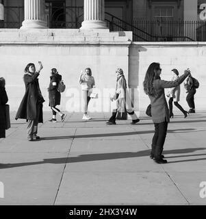 Londres, Grand Londres, Angleterre Mars 08 2022: Femme passant devant la National Gallery plusieurs prenant des selfies à l'International Womens Day. Banque D'Images