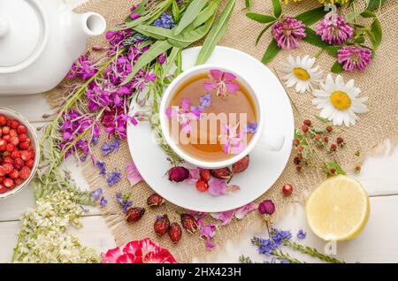 Tisane au rosehip, camomille et citron dans une tasse blanche sur une table blanche en bois avec fleurs, plat Banque D'Images