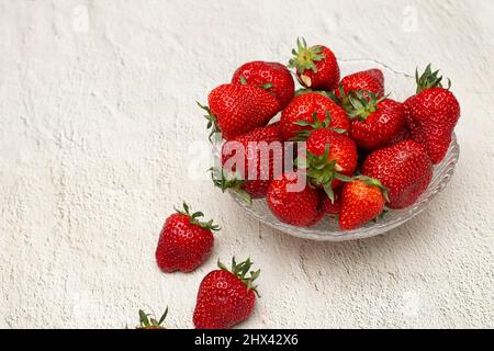 Fraises mûres dans un bol en cristal qui se tient sur une table blanche Banque D'Images