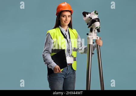 Arpenteur géodésique femelle posant avec un instrument de mesure sur un trépied isolé sur fond bleu Banque D'Images