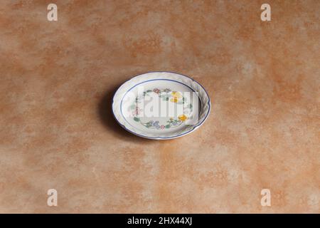 Ancienne assiette en céramique vide décorée de motifs floraux et de fruits colorés sur un fond en pierre de marbre pour une présentation élégante des aliments. Photo de studio Banque D'Images