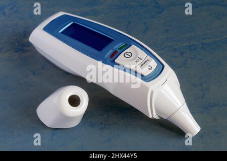 Thermomètre infrarouge pour le front et les oreilles avec écran LCD et alarme de fièvre isolé sur un arrière-plan de studio texturé porté coloré. Médecine et technologie. Banque D'Images