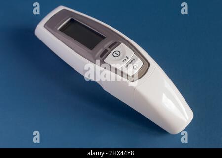 Thermomètre laser frontal et auriculaire avec écran LCD et alarme de fièvre sur fond bleu studio. Médecine et technologie. Banque D'Images