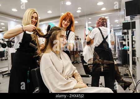 Stylistes professionnels peignant les cheveux d'une jeune femme dans le salon de beauté. Banque D'Images