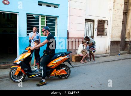 Deux femmes s'embrassent avec un baiser tandis qu'un homme avec son fils joue sur une moto à la Havane, Cuba. Banque D'Images