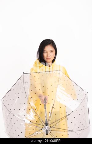 Photo de studio d'une femme asiatique avec de longs poils noirs portant un imperméable jaune et tenant vers l'avant transparent avec un parapluie à points noirs avec copie Banque D'Images