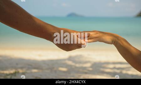 Mains de flirter jeune homme et femme touchant sur la plage dans l'ombre des palmiers contre calme azur océan vue proche. Voyager dans les pays tropicaux Banque D'Images