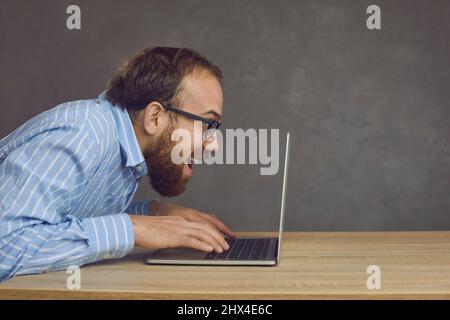 Drôle d'homme de caucasien taper rapidement sur le clavier d'ordinateur portable jouer au jeu vidéo en studio Banque D'Images