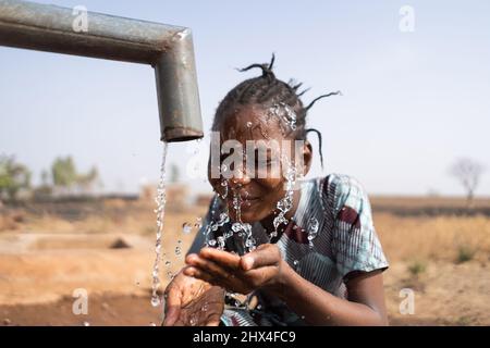 Gros plan d'une belle fille africaine se lavant le visage au point d'eau de la communauté publique ; problème social de pénurie d'eau et de distribution inadéquate Banque D'Images