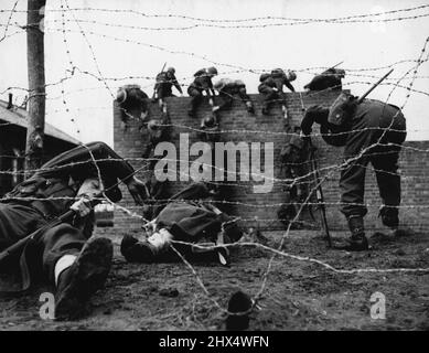 Le cours d'assaut « durcissant » et les exercices d'endurcissement de l'Armée -- l'image montre passer par un obstacle de fil barbelé, avec d'autres hommes au-delà de la mise à l'échelle d'un mur de dix pieds. Des photos illustrant la gravité de l'entraînement de durcissement du personnel de l'armée pris lors d'un cours d'assaut moderne où de nouvelles méthodes ont été introduites. Toutes les classes de personnel militaire - infanterie, artillerie, unités médicales, équipes de chars, signaux, etc. suivre la formation. 24 mars 1942. (Photo par British Official Photograph). Banque D'Images