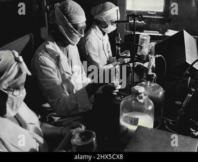 Photographie par Hans Reinhart -- femmes en blanc......portant des masques aseptiques, des casquettes et des robes, des femmes techniciens au W.H. Les laboratoires de parc travaillent dans des armoires stériles. Ils remplissent les flacons avec le vaccin antirabic. Ce produit a sauvé la vie de nombreuses personnes mordues par des animaux enragés. 27 juillet 1941. (Photo par International News photos). Banque D'Images