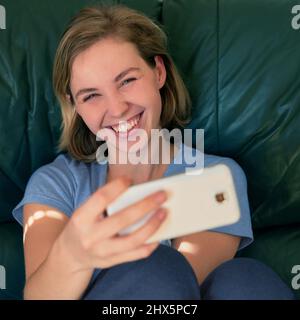 Mais d'abord, laissez-moi prendre un selfie. Photo d'une jeune femme heureuse prenant un selfie avec son téléphone à la maison. Banque D'Images