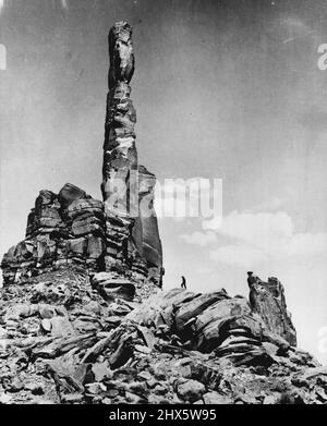 Un homme (au centre) apparaît comme une figure insignifiante lorsqu'il se rend sur les rochers massifs qui mènent au plus haut des totems de Monument Valley dans l'Utah. Bien que d'autres rochers à proximité se soient effondrés, cette grande flèche reste à une hauteur de 1006 pieds au-dessus du sol et jette une ombre de 35 miles à travers le désert à Sundown. 29 août 1952. (Photo de United Press). Banque D'Images