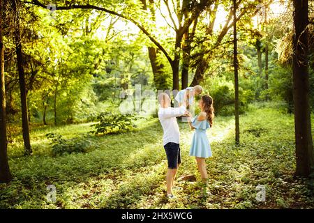 Famille aimante marchant dans le parc, forte remontée de père dans l'air bébé fille, adorable mère tient dans les bras petites filles jambes, souriant, heureux Banque D'Images