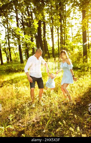 Les jeunes parents jouent avec une petite fille, un père souriant, attentionné et aimant lève-maman dans l'air adorable petite fille, jeune famille marchant dans le parc, profiter Banque D'Images