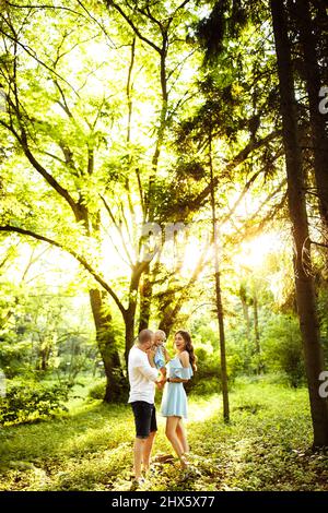 Une jeune famille surjoyeuse marchant dans le parc, des parents attentionnés jouent avec une petite fille, un père souriant et aimant tient une adorable petite fille dans les bras, profiter Banque D'Images