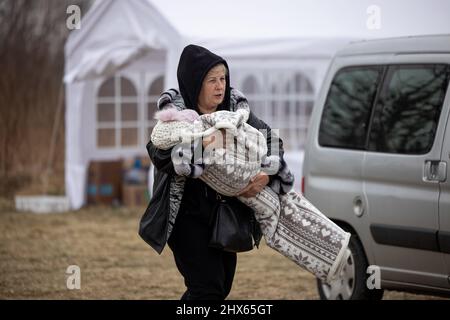 Przemysl, Pologne. 09th mars 2022. Une femme a vu porter son jeune enfant à l'extérieur du centre d'accueil des réfugiés.Un centre d'accueil temporaire des réfugiés a été installé dans un ancien entrepôt de Tesco, à la périphérie de Przemy?l, pour abriter des centaines de milliers de réfugiés ukrainiens qui fuient par la frontière entre Medyka et Shehyni. Crédit : SOPA Images Limited/Alamy Live News Banque D'Images