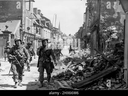 Les troupes américaines à Carentan -- les troupes américaines gardent un œil prudent sur les tireurs d'élite alors qu'ils font pression sur les bâtiments qui ont été épatés dans une rue de Carentan. Ce centre de communication clé sur la péninsule de Chorbourg est tombé aux troupes aériennes américaines après un important bombardement par les alliés. 1 août 1944. (Photo par photo de presse associée). Banque D'Images