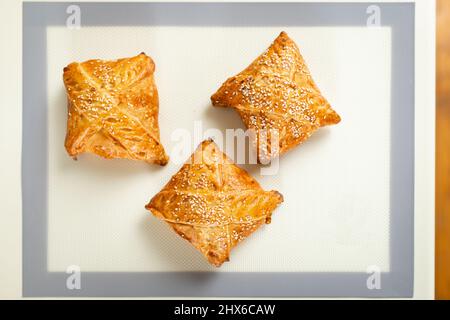 Vue de dessus de samsa fraîchement cuit sur le tapis de cuisson sur la table de cuisine. Banque D'Images