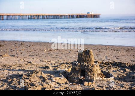 Château de sable de deux étages décoré de coquillages sur la plage d'Avila, avec jetée en arrière-plan. Banque D'Images