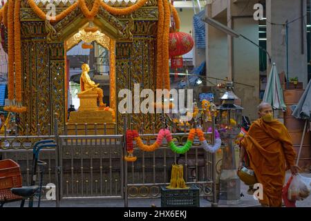 Au Pak Klong Talat (marché) à Bangkok, en Thaïlande, un moine bouddhiste passe devant un sanctuaire en l'honneur d'un ancien fonctionnaire considéré comme l'esprit gardien du marché Banque D'Images