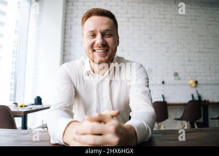 Portrait en gros plan d'un beau jeune homme d'affaires heureux assis au bureau dans une salle de bureau moderne et souriant regardant l'appareil photo. Banque D'Images