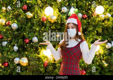 Femme en masque médical et chapeau de père noël avec arbre de Noël, coronavirus (covid-19) et x-mas célébrant concept Banque D'Images