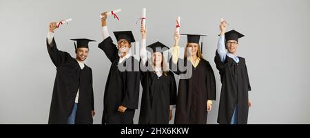 Joyeux succès multiracial diplômés avec des manuscrits de diplômes en mains sur fond gris. Banque D'Images