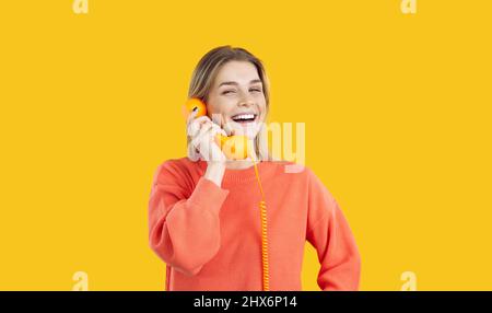 Portrait d'une jeune femme joyeuse parlant sur un téléphone fixe isolé sur fond jaune. Banque D'Images